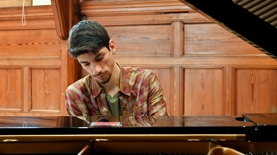 Male student playing the piano in the Parry rooms, a wooden panelled room.